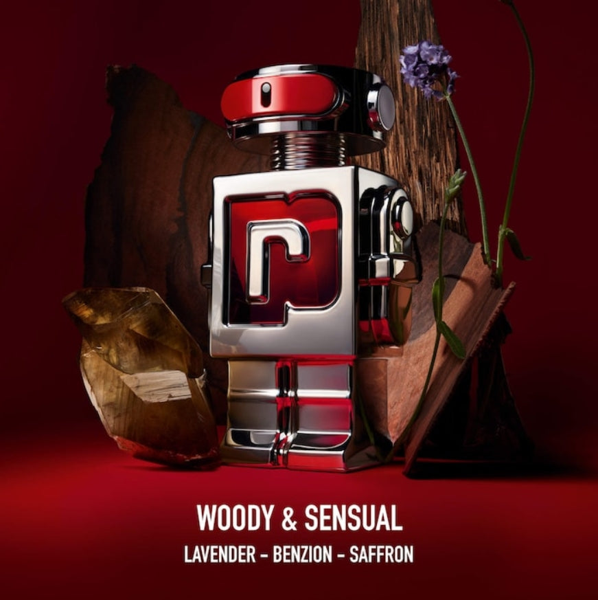 A perfume bottle with a metallic silver and red robot-like design, styled with a dark red background, wood props, a crystal, and a purple flower. Text at the bottom reads 'WOODY & SENSUAL', 'LAVENDER - BENZON - SAFFRON'.
