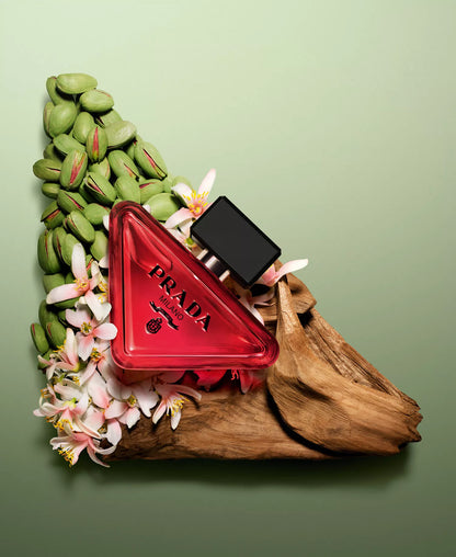 Red Prada triangle-shaped perfume bottle with green beans and flowers on a green background