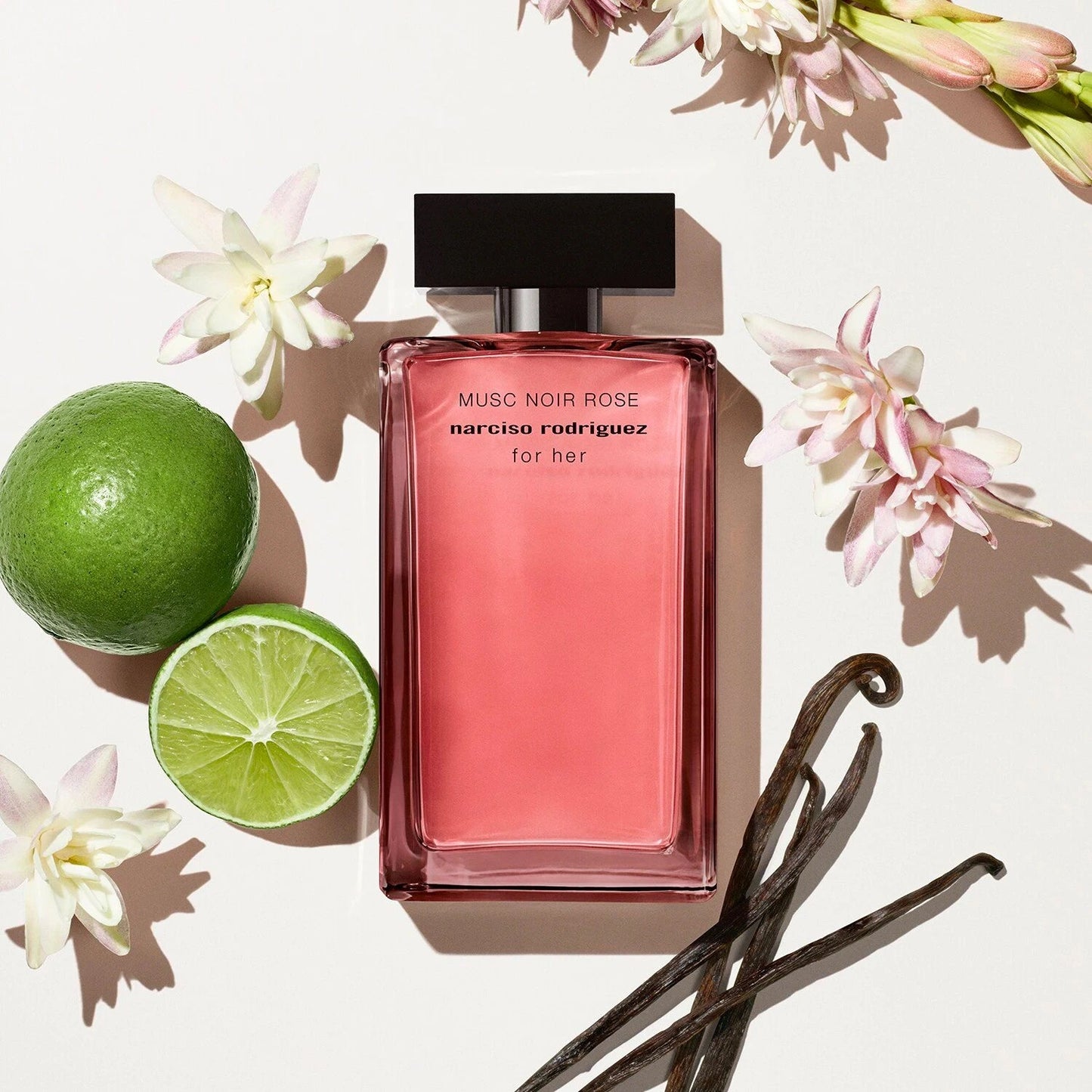 Pink perfume bottle with flowers, lime, and vanilla beans on a light background