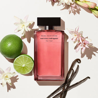 Pink perfume bottle with flowers, lime, and vanilla beans on a light background