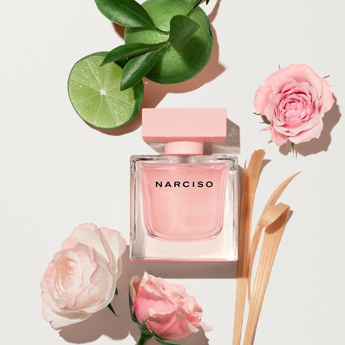 Pink Narciso perfume bottle with flowers and a lime on a light background