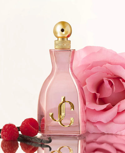 Perfume bottle with gold cap and logo, pink flower, and raspberries on a light background