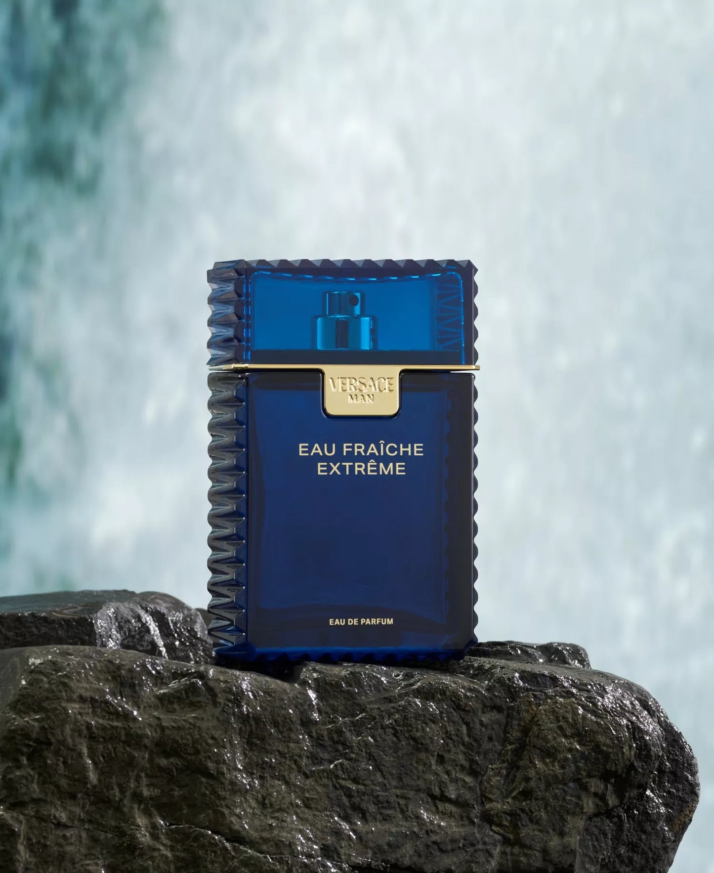 Blue perfume bottle labeled 'Eau Fraiche Extreme' on a rock with waterfalls in the background