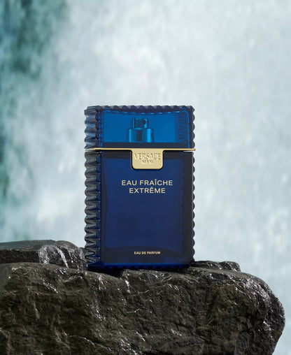 Blue perfume bottle labeled 'Eau Fraiche Extreme' on a rock with waterfalls in the background